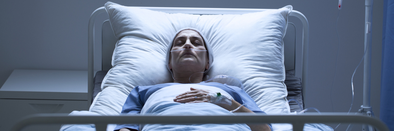 An older white woman in a hospital bed sleeping, dark room