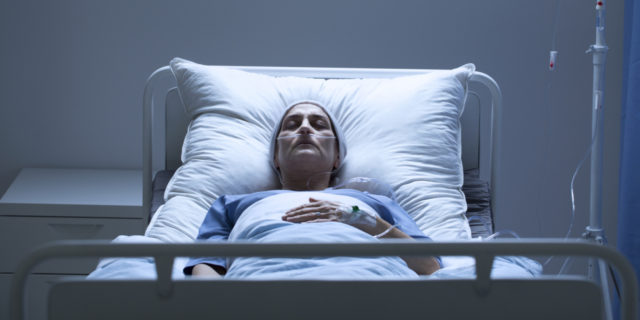 An older white woman in a hospital bed sleeping, dark room