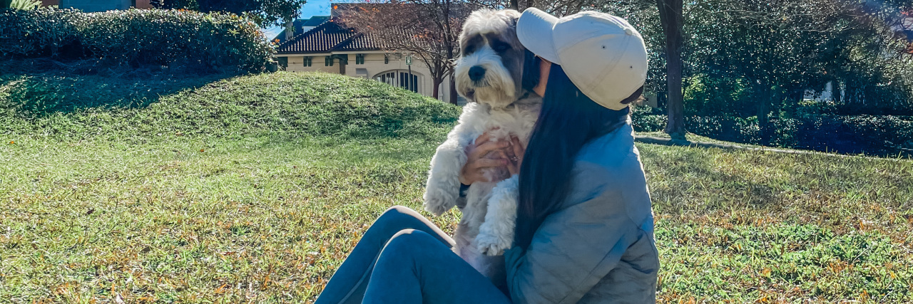 a woman sitting on a lawn snuggling her dog