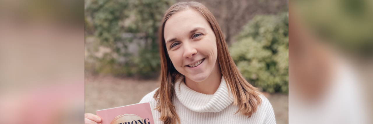 Overcoming Anxiety Presented as Perfectionism and People-Pleasing Photo of author Kelsey Buckholtz, a young white woman with ginger hair smiling outside holding her book