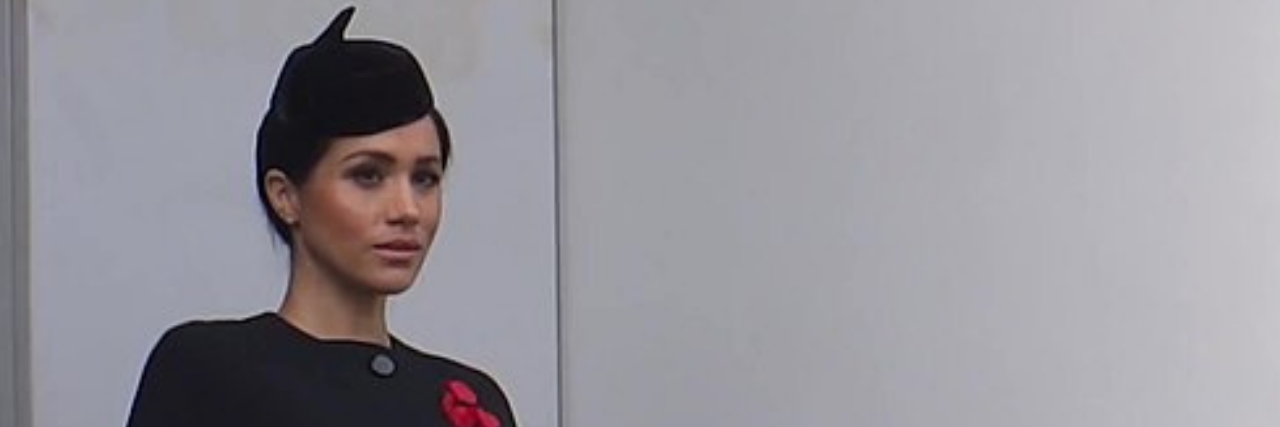 The Royal Family on Meghan Markle's Suicidal Thoughts Calls for Change Meghan Markle dressed in black with a red pin on her chest looking out