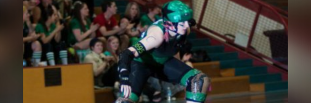 Photo of author, young white woman, playing roller derby in a gym filled with fans