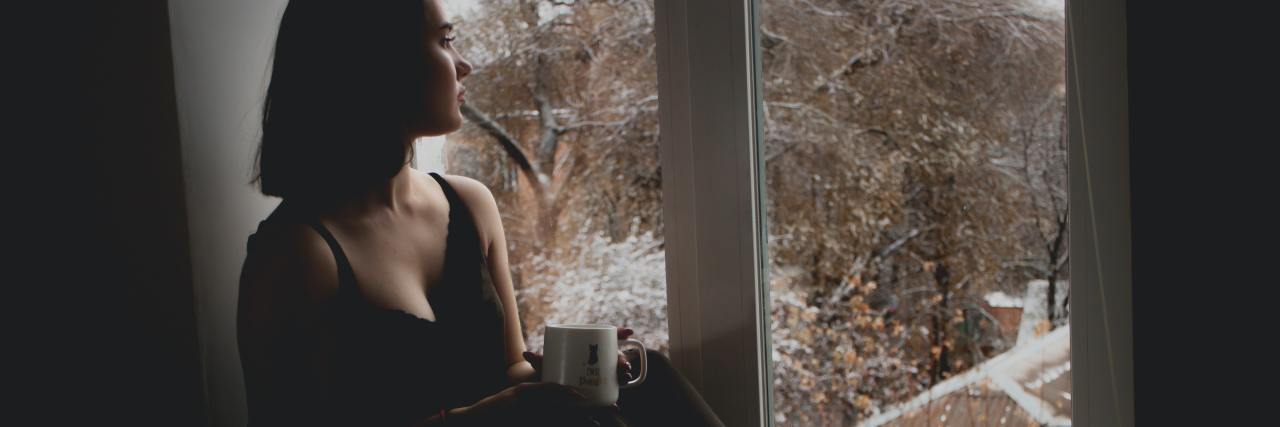 Stigmatizing Mental Health Phrases We Should Stop Using photo of a woman in low light sitting on windowsill, looking outside