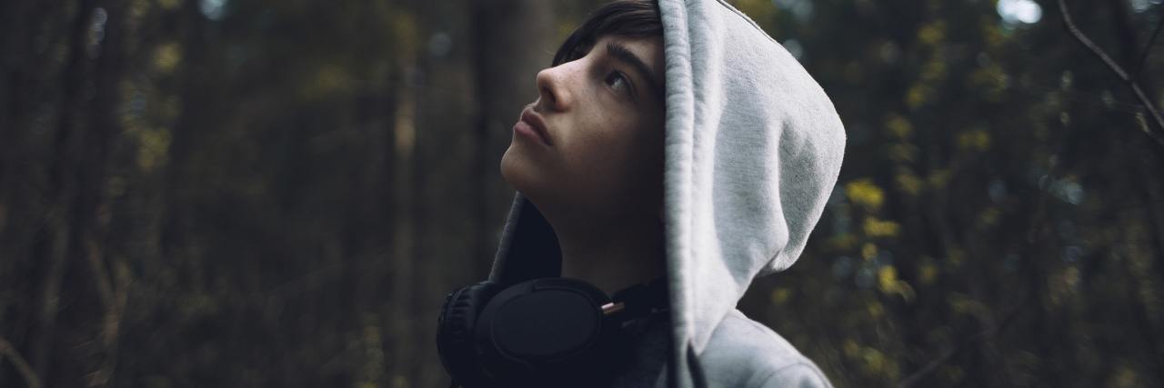 photo of a young teenage boy wearing a hooded sweatshirt and looking up at trees in a forest