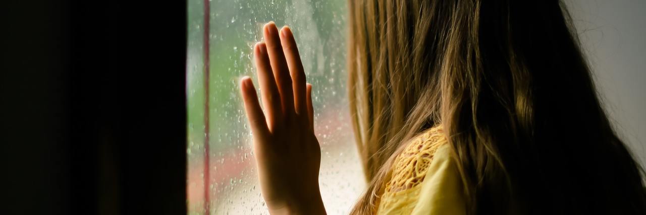 How Heartbreak Led to My Borderline Personality Disorder Diagnosis photo of woman looking out of window with hand pressed to glass, facing away from camera