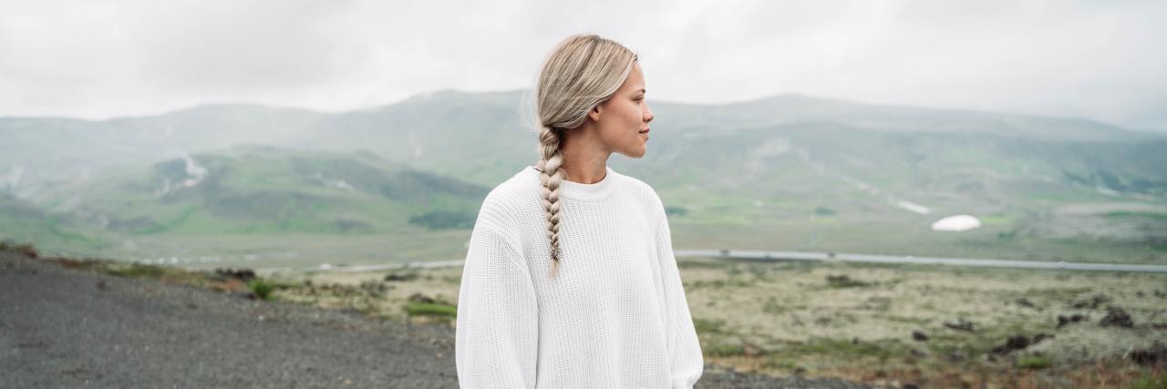 I'm Diagnosed With PTSD, but My Trauma Doesn't Feel 'Bad Enough' A white woman standing on a beach with her hair in a braid, looking off