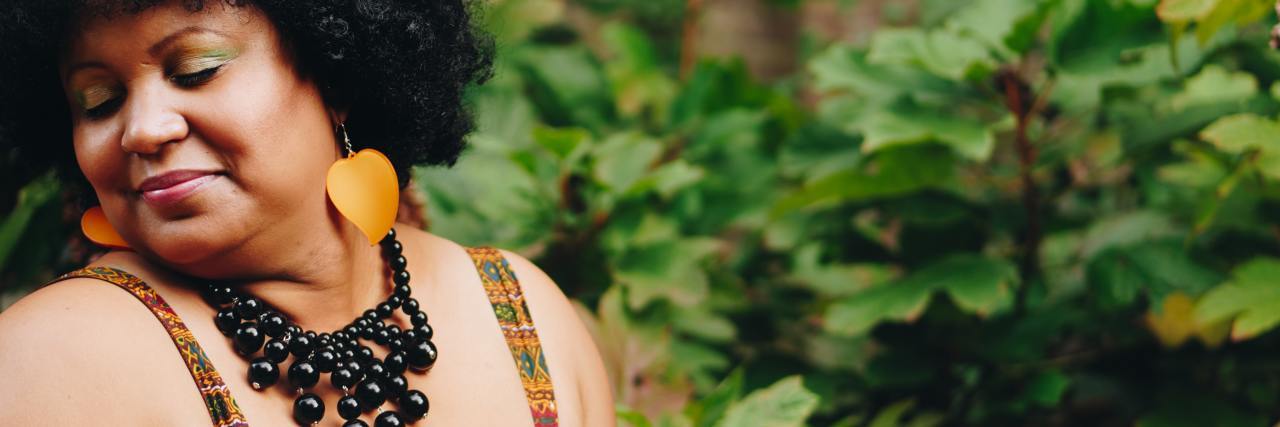 I’m Liberating Myself From Diet Culture and Loving My Black Body photo of a plus size black woman looking happy and smiling, posing outdoors in sunlight
