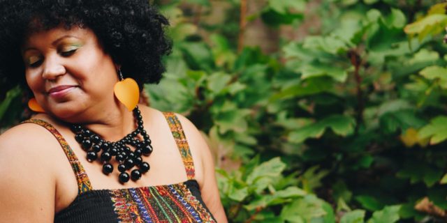 I’m Liberating Myself From Diet Culture and Loving My Black Body photo of a plus size black woman looking happy and smiling, posing outdoors in sunlight
