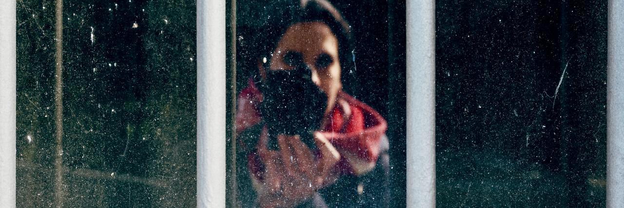 photo of a woman taking a self-portrait in a window with mountains behind her