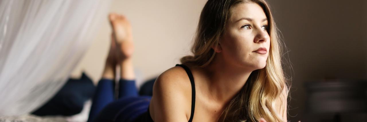 Can I Find Love If I Have Bipolar Disorder? photo of a woman lying on a bed on her stomach looking hopefully out of window