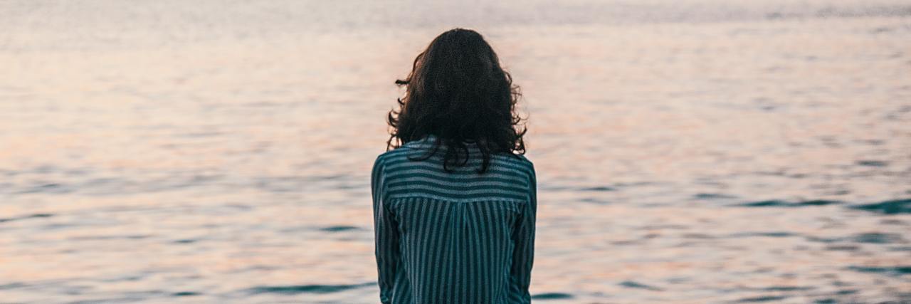 A woman with long black hair standing in front of an ocean at sunset