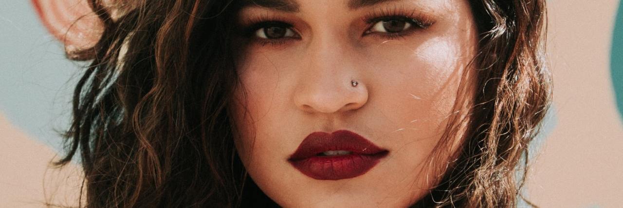 Why Calling Borderline Personality Disorder Manipulative is Harmful close up of a woman looking into the camera with red lipstick and a serious expression, her hand raised to her collar
