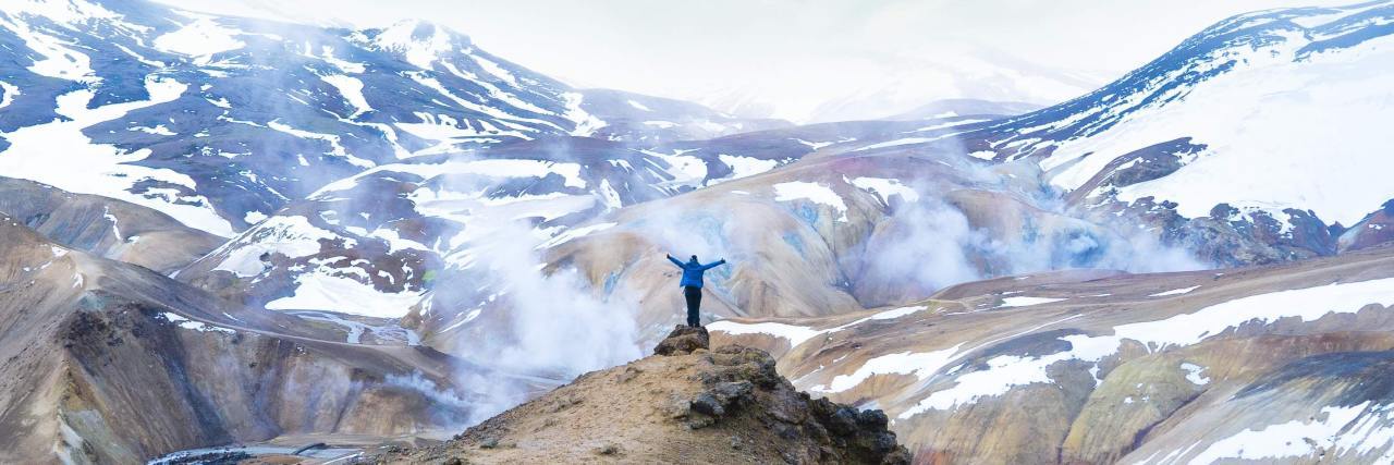 Chronic Pain and Mental Illness Makes It Hard to Trust Myself photo of someone standing on a rock overlooking a valley and mountains in Iceland, arms outstretched to the sky