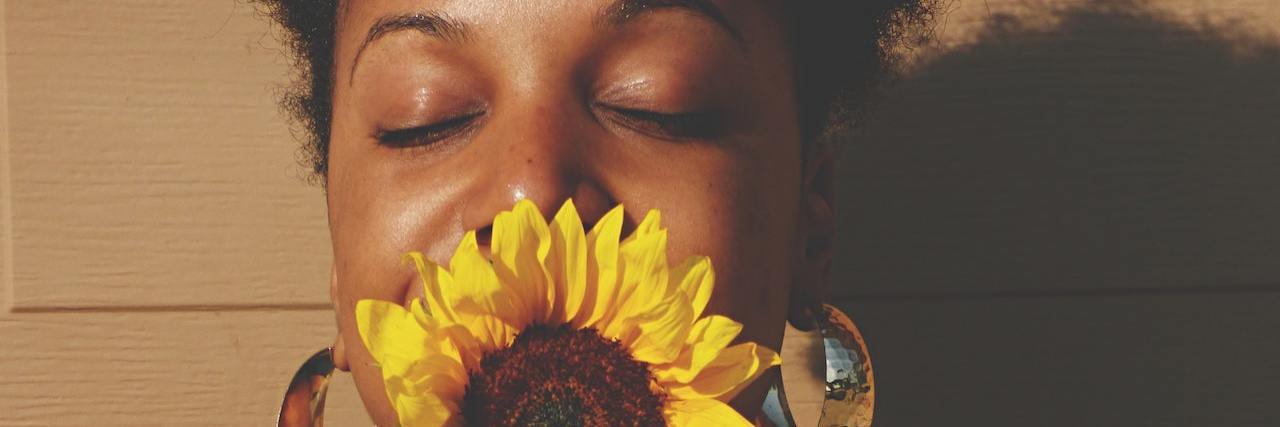 A Black woman with a sunflower in front of her face