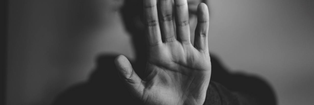 The Good and Bad of Being in Denial About an Abusive Relationship black and white photo of a woman holding her outstretched hand in a stop pose, covering her face