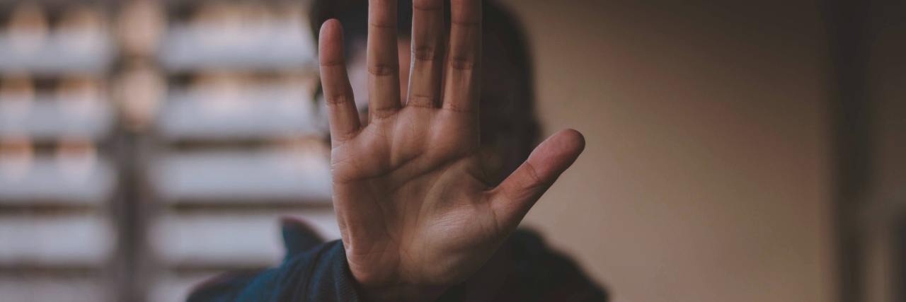 Mental Health: How to Set Boundaries Without Explaining Yourself photo of person with focus on their hand, holding it out in stop sign for the camera, covering their face