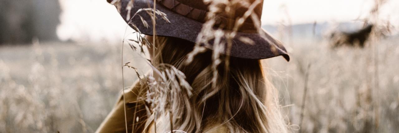 Types of Internal and External Scars With Mental Illness photo of a woman in a field, facing away with hand raised on her neck, among long grass or crops