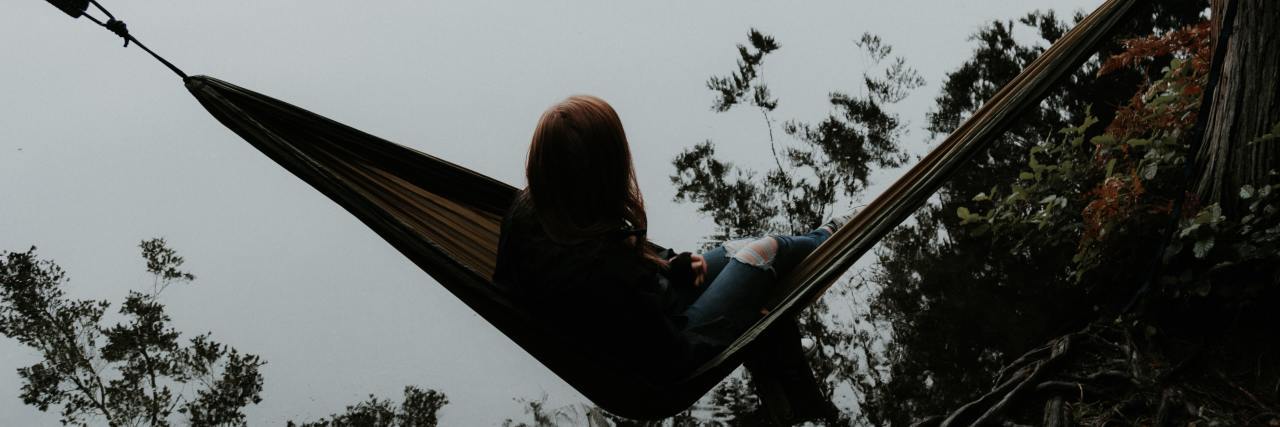 A young woman siting on a hammock overlooking the mountains