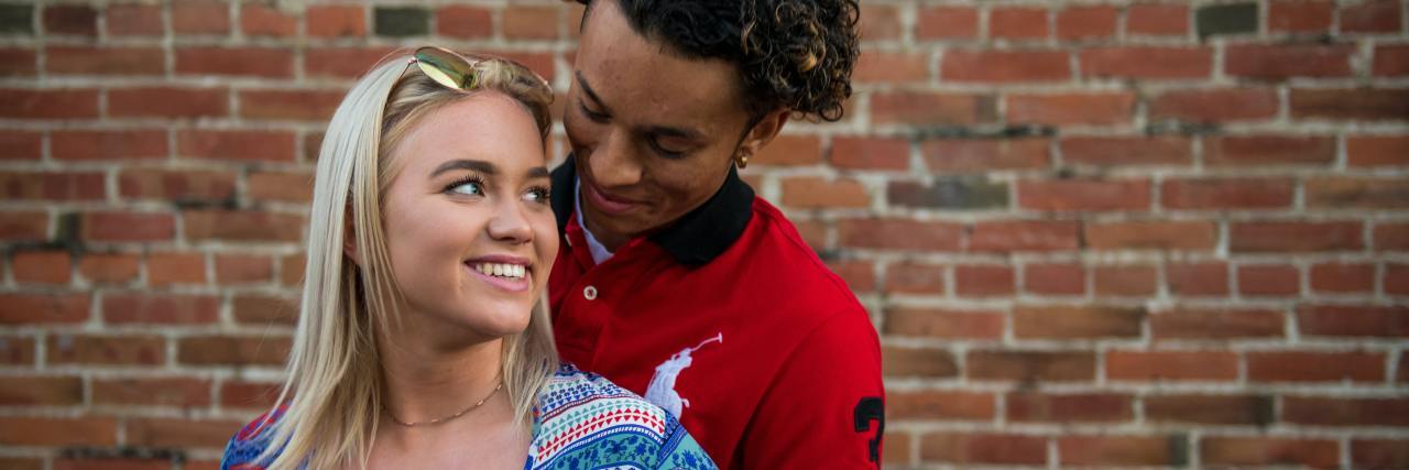 Dating: When Do You Tell Someone You Have Bipolar Disorder? photo of a young man and woman with a backdrop of a brick wall, looking into each others' eyes and smiling