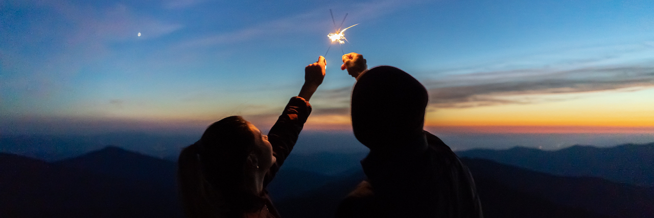 A couple holds sparklers together at sunset