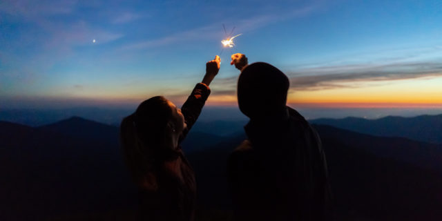 A couple holds sparklers together at sunset