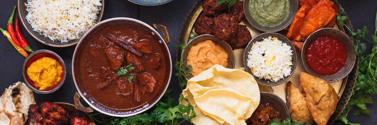 Learning to Cook Again After Becoming Blind Various Indian dishes featuring rogan josh, chicken tikka masala, biryani, tandoori chicken, kebabs and mixed indian platter with samosa, pakoras, onion bajis, poppadoms , naan and dips, top view