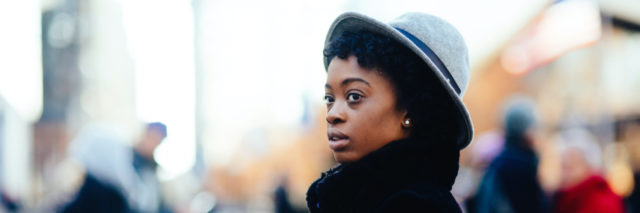 Portrait of a Black woman in faux fur coat and stylish hat walking on a busy big city street