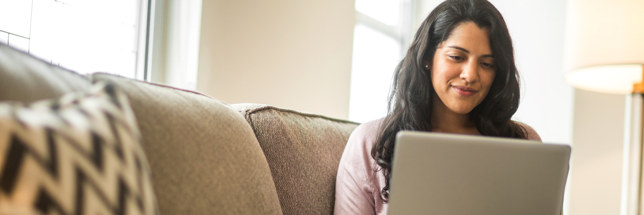 A woman with brown skin sitting on a couch and using her computer