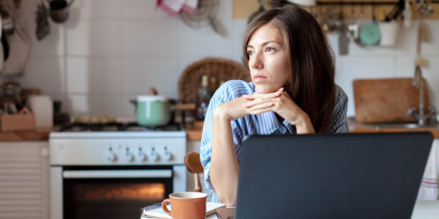 Woman sitting at kitchen table in front of a laptop, looking to the side