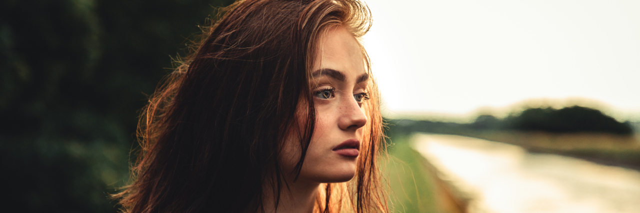 What Living With Chronic Pain as a Teenager Is Really Like A young, white girl with red hair standing outside looking away, sad