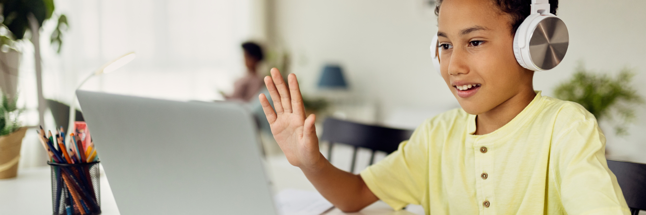 Why Remote Learning Works for My Son With Autism African American boy using laptop and waving during video call while homeschooling.