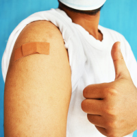 A man holding up a thumbs up with a bandage on his arm after getting the covid-19 vaccine
