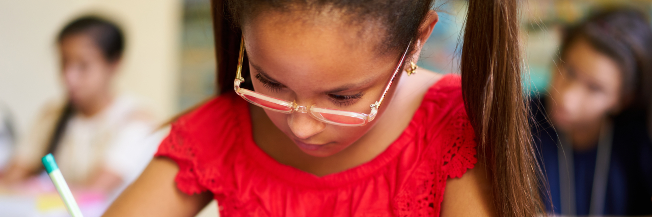 Does my Daughter Have ADHD? a young girl writing at a desk in a classroom