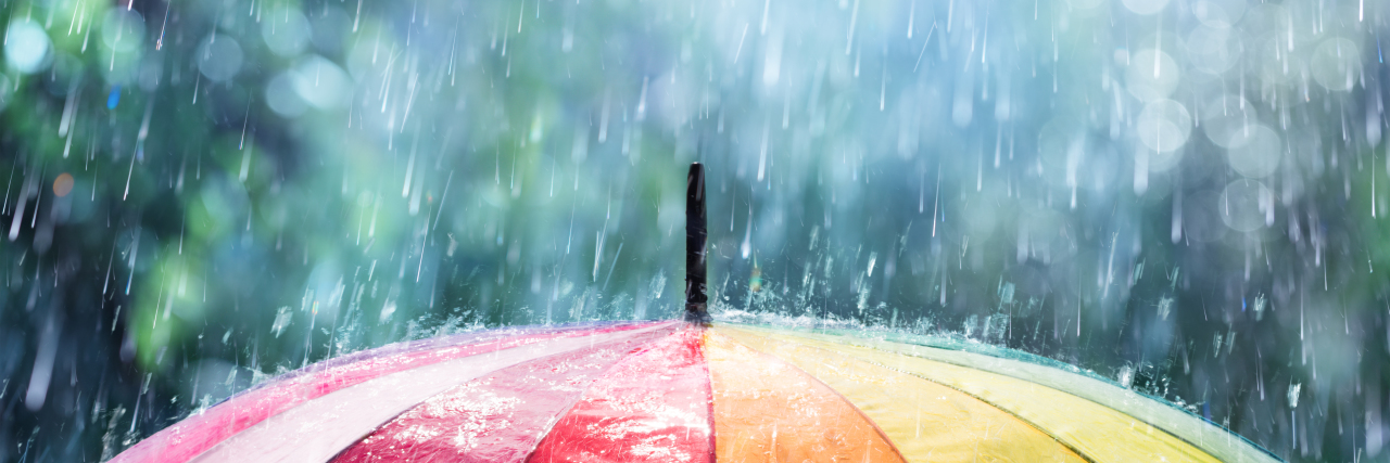 Why Many Autistic People Don't Celebrate Autism Awareness Month Rain falling on rainbow umbrella.