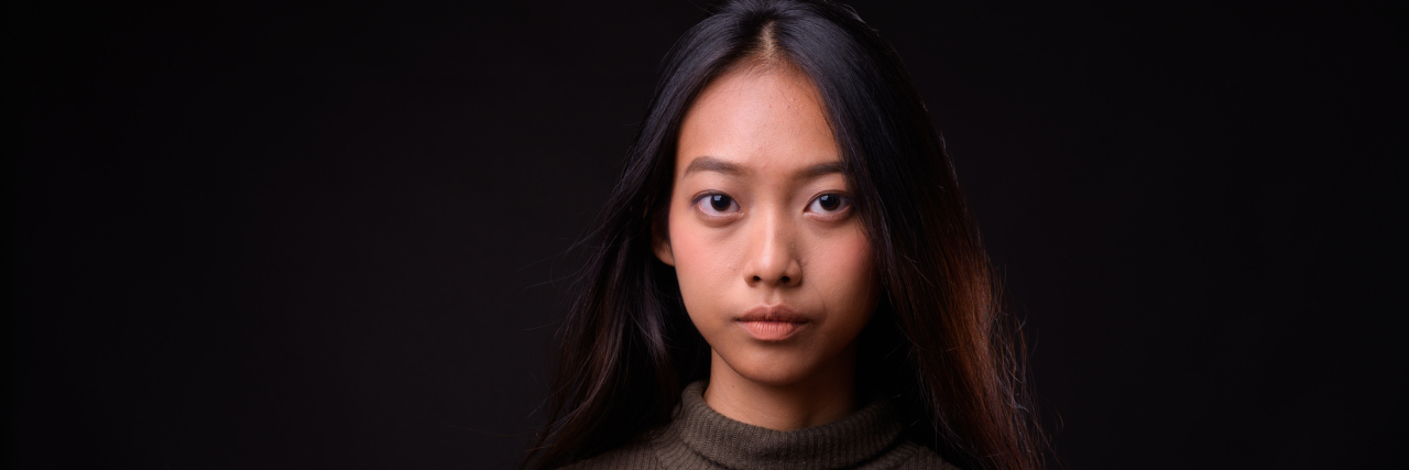 A young Asian woman with a serious face looking into the camera against a black background