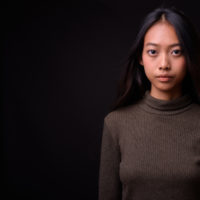 A young Asian woman with a serious face looking into the camera against a black background