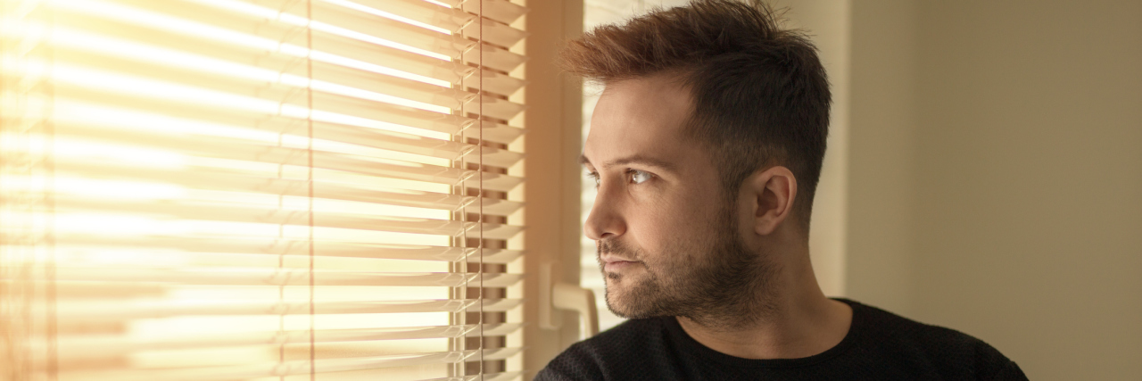How to Create a Good Morning Routine to Improve Mental Health Young man standing by the window drinking a cup of coffee, looking outside