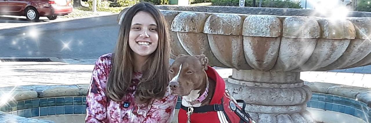 Training My Own Psychiatric Service Dog as a Teen Jennica sitting by a fountain with her service dog, a brown pit bull.