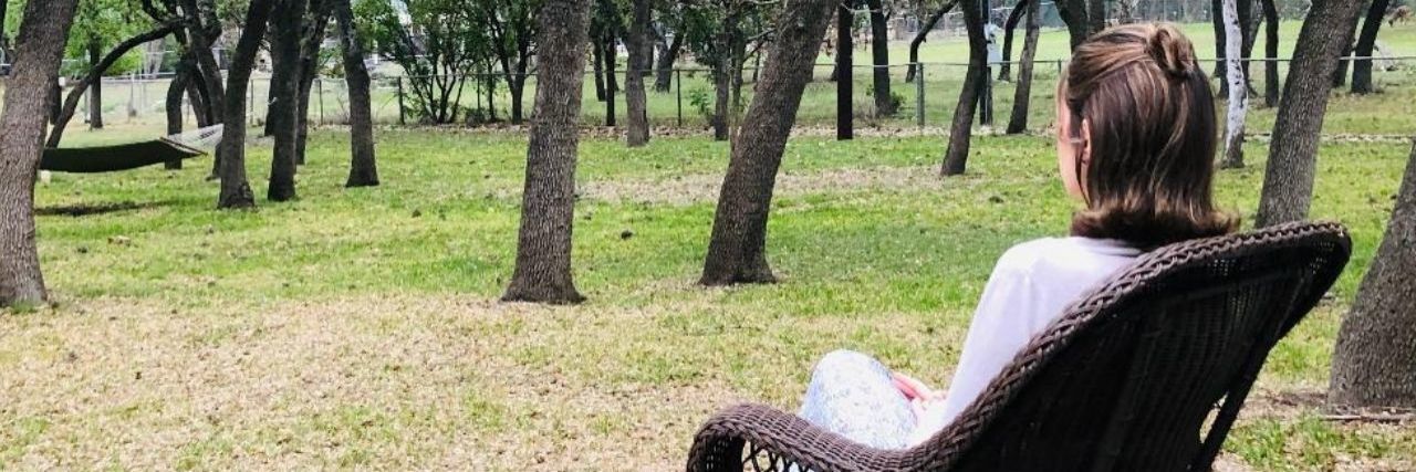When Your Identity Is Stripped Away by Chronic Illness a young woman sitting on a rocking chair on a porch looking at a field of trees
