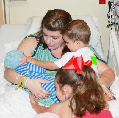 Photo of author, white woman in a hospital bed holding her newborn baby with her young son and daughter on the bed
