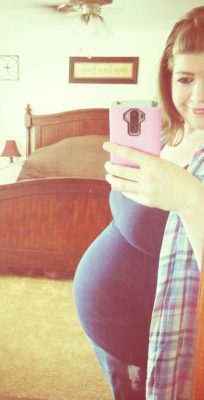 Mirror selfie of the author, a white woman with brown hair, when pregnant, smiling