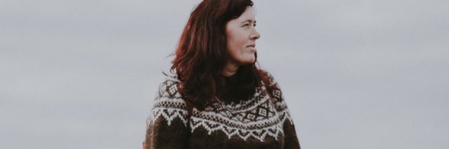 photo of a woman in a sweater standing in a field and looking into the distance