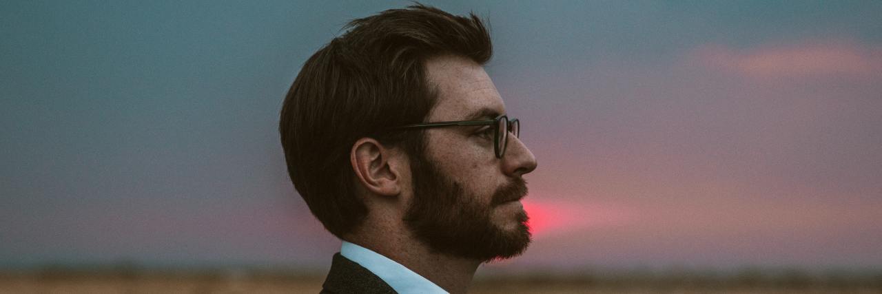 Side profile of a young white man in a suit and glasses at sunset