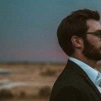 Side profile of a young white man in a suit and glasses at sunset