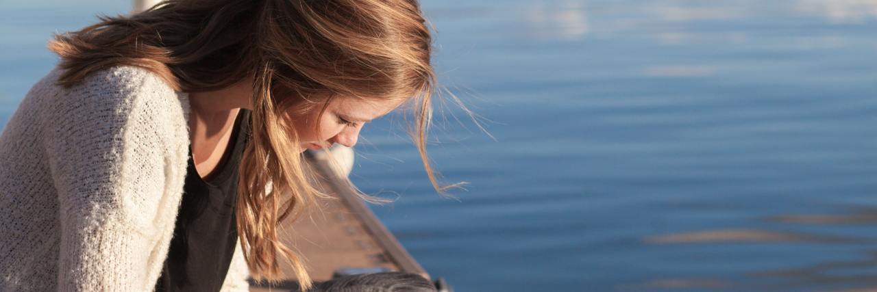 photo of a woman reading on a dock with water behind her
