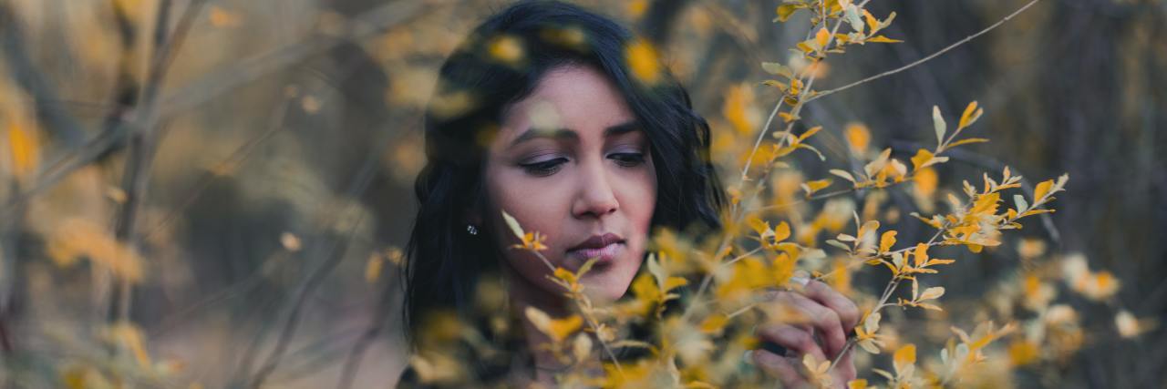 A young Asian woman surrounded by trees with yellow leaves, looking off