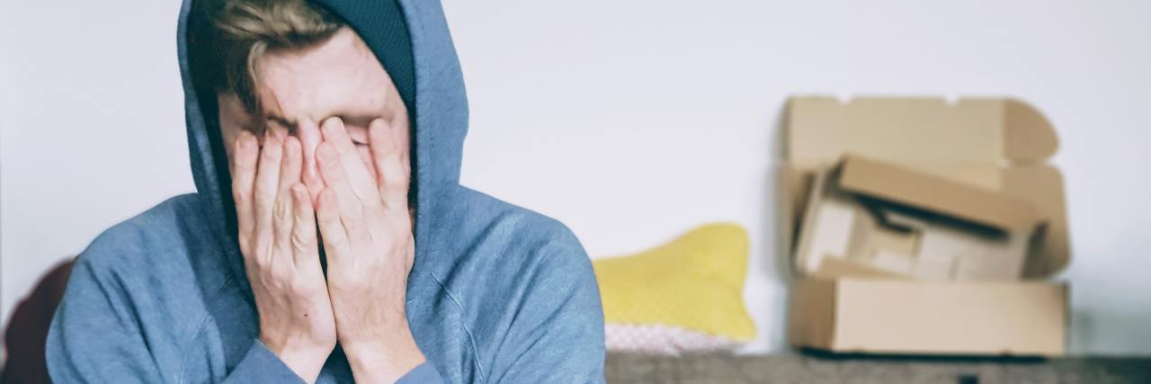 Shame at Needing to Tell Work You're Struggling With Depression photo of a man sitting on a couch with his hands over his face and eyes