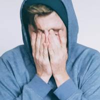 photo of a man sitting on a couch with his hands over his face and eyes