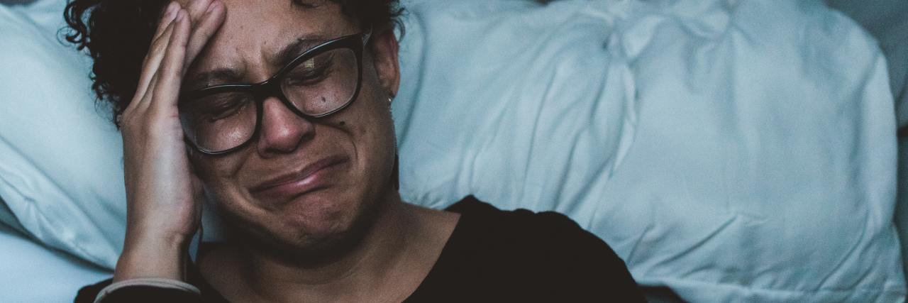 photo of a woman crying and upset while kneeling beside bed, her head in her hand