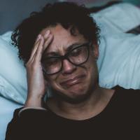 photo of a woman crying and upset while kneeling beside bed, her head in her hand